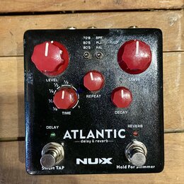 Černý efekt pedál s červenými ovládacími knoflíky. Na spodní části je bílý nápis ATLANTIC — delay & reverb — a logo NUX. Pedál obsahuje dva spínače s…