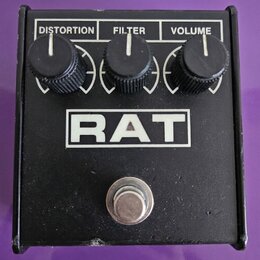 Kytarový efekt v černém kovovém šasi. Na horní straně jsou tři černé oválové knoflíky s popisky DISTORTION, FILTER a VOLUME. Uprostřed je bílý obdéln…