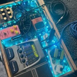 Dřevěný kufr s pedalboardem, který je podsvícen modrými LED pásky. Obsahuje efektové pedály a procesor s nápisy „BOSS“, „MB-800“ a „MAH SUP“. V kufrě…