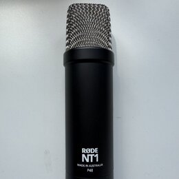 Černý kondenzátorový mikrofon s kovovou stříbrnou mřížkou. Na spodní části těla je bílý nápis RØDE NT1 a pod ním text MADE IN AUSTRALIA P48. Povrch m…