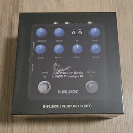 Fotografie znázorňuje krabici s basovým předzesilovačem NUX. Na zařízení jsou vidět ovládací knoflíky s popisky VOLUME, BLEND, IR, DRIVE, BASS, MIDDL…