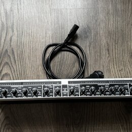 Stříbrný rackový procesor s černými ovládacími prvky a nápisem COMPOSER PRO-XL. Na pravé straně je logo behringer a vypínač POWER. Za přístrojem leží…
