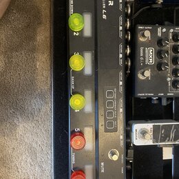 Černý MIDI kontrolér s nápisem MOOER PEDAL CONTROLLER L6. Zařízení má čtyři žlutá a dvě červená zapadací tlačítka, z nichž některá jsou popsána nápis…