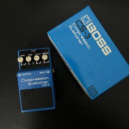 Modrý efekt pedál značky BOSS s nápisem Compression Sustainer CS-3. Na horní části jsou čtyři ovládací knoflíky s popisky LEVEL, TONE, ATTACK a SUSTA…