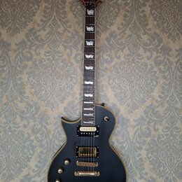 Černá elektrická kytara typu singlecut s hnědým lemováním. Na hlavě je zlaté logo Ltd a nápis ESP. Kytara má dva humbuckery se zlatými kryty, zlatý m…