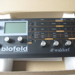 Šedý desktopový syntetizátor s nápisy blofeld SYNTHESIZER a waldorf. Přístroj má displej, několik ovládacích knoflíků a řadu tlačítek s popisky jako…
