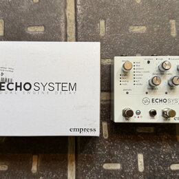 Bílá krabice a efekt pedál s bílým povrchem. Na obou je černý nápis ECHO SYSTEM DUAL ENGINE DELAY a logo Empress. Pedál obsahuje několik ovládacích k…