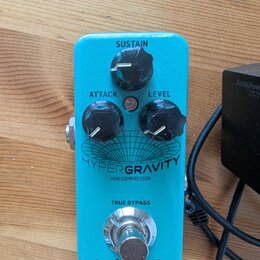 Modrý kytarový efekt s nápisy HYPERGRAVITY a MINI COMPRESSOR. Na horní straně jsou tři černé otočné ovladače s popisky SUSTAIN, ATTACK a LEVEL. Ve sp…