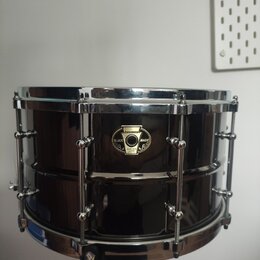 Černý malý snare drum s chromovaným kováním. Na koruse je umístěn oválný štítek s nápisy „pawpaw“, „BLACK MAGIC“ a „SNARE DRUM LIMITED“. Povrch nástr…