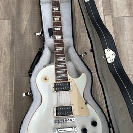 Bílá elektrická kytara s tvarem singlecut v černém etuši s bílou vnitřní výplní. Na hlavě je viditelné logo Gibson. Kytara má dva humbuckery, světle…