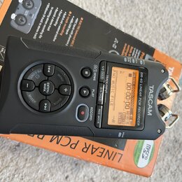 Černý digitální nahrávač TASCAM DR-40 LINEAR PCM RECORDER s displejem a ovládacími tlačítky. Zařízení leží na oranžovém originálním obalu. Na horní s…