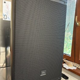 Černý aktivní reproduktor s kovovou mřížkou v horní a spodní části. V dolní části mřížky je umístěno logo JBL. Povrch přístroje i mřížka vykazují zná…