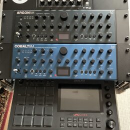 Fotografie zobrazuje čtyři hudební zařízení v racku. Shora dolů jsou vidět moduly Moog MINITAUR, Argon8M a Cobalt8M v modré barvě, a ve spodní části…