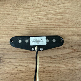 Černý elektrický snímač s šesti viditelnými bílými póly. Uprostřed je nalepená bílá nálepka s logem a nápisem Fender Custom Shop. Z spodní části vedo…
