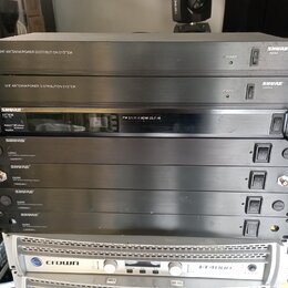Snímek zachicuje stoh rackových zařízení. V horní části jsou dvě šedé jednotky s nápisem UHF ANTENNA/POWER DISTRIBUTION SYSTEM a logem SHURE UA844. P…