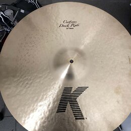 Zlatavý činely s kovaným povrchem. Na horní části je nápis Custom Dark Ride a 22"/56cm, ve spodní části je velké černé logo K. Povrch vykazuje drobné…