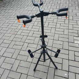 Černý stojan na kytaru s třemi rameny zakončenými oranžovými gumovými kryty. Stojan má teleskopický středový sloup a trojnožku s gumovými koncovkami.…