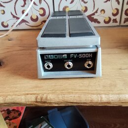 Stříbrný expresní pedál s dvěma šedými plochmi pro nohu. Na zadní straně je nápis BOSS FV-500H a tři konektory označené jako INPUT, OUTPUT a EXP. Pov…