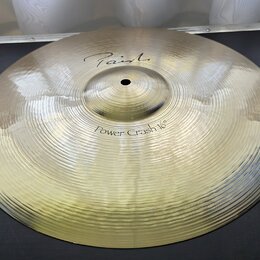 Zlatavý kovový činel s viditelným rýhováním po celém povrchu. Na horní části je nápis "Paiste" a níže označení "Power Crash 16"". Povrch je čistý a b…