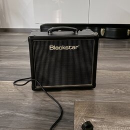 Černý kytarový kombo zesilovač s rukojetí nahoře a černou síťovkou. Na přední straně je bílý nápis Blackstar®. Z přístroje vede napájecí kabel s vidl…