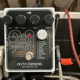 Bílý efekt pedál s černým předním panelem a nápisem bass machine 9:9. Na spodní části je logo electro-harmonix NEW YORK CITY, USA. V horní části jsou…