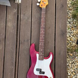 Vícestrunná elektrická basová kytara v tmavě červené barvě s bílým pickguardem. Na hlavě hmatníku je viditelné logo Fender. Nástroj má dřevěný hmatní…