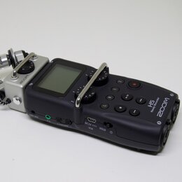 Černý digitální záznamový přístroj s LCD displejem a stříbrným kovovým rámem kolem mikrofonů. Na přístroji jsou bílé nápisy ZOOM, H5 Handy Recorder,…