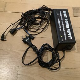 Černý napájecí adaptér s nápisem MULTI POWER SUPPLY. Na boku je uveden text SEPARATE ISOLATED 6x DC10V/100mA & 2x DC10V/200mA - SMRCKAEFFECTS - a ozn…