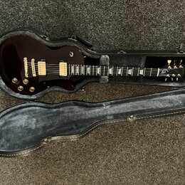 Tmavě hnědá elektrická kytara s bílým ráfkem v černém tvrdém kufru. Na hlavě kytary je viditelné logo Gibson. Nástroj má dva humbuckery, zlatý hardwa…