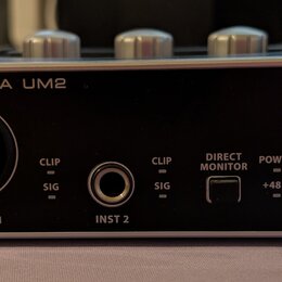 Černý zvukový interface s kovovým stříbrným rámem. Na přední straně jsou nápisy U-PHORIA UM2 a logo behringer, vstup MIC/LINE 1 s nápisem XENYX MIC P…