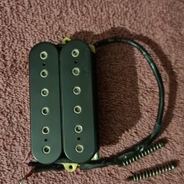 Černý humbucker s dvěma řadami šesti polových magnetů. Na spodní části levého snímače je svisle napsaný nápis DiMarzio. K nástroji vedou černé vodiče…