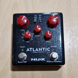Kytarový efekt pedál s černým třpytivým povrchem a červenými ovládacími knoflíky. Na spodní části je bílý nápis ATLANTIC delay & reverb a logo NUX. V…
