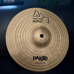Kruhový mosazný činel s koncentrickým žebrováním povrchu. Na horní části je logo Paiste a nápis ALPHA, ve spodní části je nápis PAiste a pod ním SPLA…