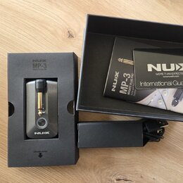 Na fotografii je malý kytarový zesilovač v originálním černém balení. Na krabici i na přístroji je bílý nápis NUX a označení modelu MP-3 MIGHTY PLUG…