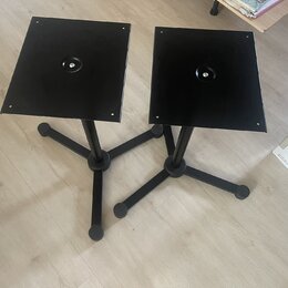 Dva černé stojany s hranatými horními deskami a trojnožkami. Na deskách jsou uprostřed kulaté otvory. V pravé části snímku je vidět část krabice s ná…