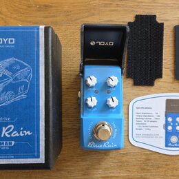 Modře lakovaný efekt pedál s nápisy Blue Rain, Overdrive a True Bypass. Na pedálu jsou tři bílé ovládací knoflíky s popisky VOLUME, TONE a HIGH. Souč…