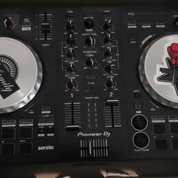 Černý DJ 컨트롤러 Pioneer Dj s logem serato v dolní části. Zařízení má dva stříbrné jog-wheels, z nichž oba jsou zakryty nálepkami; na levém je nápis The…