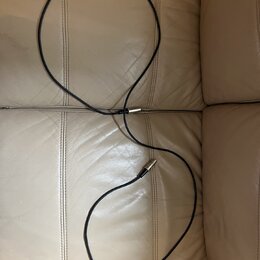 Černý instrumentální kabel s kovovými konektory. Kabel je položen na béžovém koženém povrchu. Na kabelu ani konektorech nejsou viditelné žádné značky…