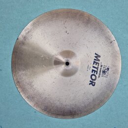 Kruhové činely z kovu stříbrné barvy s viditelným broušením. Na povrchu je modrý nápis METEOR a menší texty Made in Germany, by MEINL a Crash 14. Pov…
