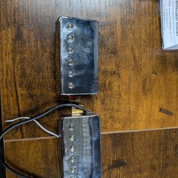 Dva elektrické kytarové snímače s chromovaným krytem a viditelnými polosnovými póly. Snímače jsou vybaveny připojovacími kabely v černé a bílé barvě.…