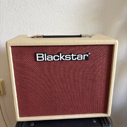 Kytarový kombozesilovač s krémovým vinylovým potahem a červenou texturovanou přední síťovkou. Uprostřed sítě je umístěno bílé logo Blackstar. Zesilov…