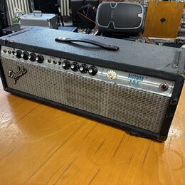 Kytarový kombozesilovač s černým texturovaným potahem a stříbrným předním panelem. Na levé straně je viditelné logo Fender a vpravo nápis BASSMAN 135…