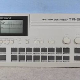 Bílý rytmický automat s displejem a ovládacími tlačítky. Na horní části je nápis RHYTHM COMPOSER TR-505 a v levém horním rohu logo Roland. Zařízení o…