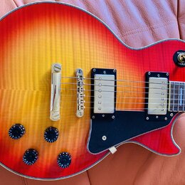 Elektrická kytara s trupem v červeno-žlutém sunburst provedení a viditnou strukturou dřeva. Nástroj má dva humbuckery s kovovými kryty, černý pickgua…