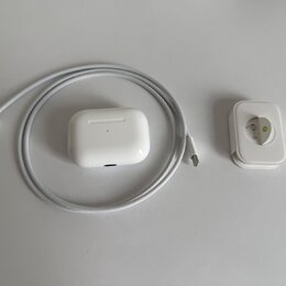 Bílé nabíjecí pouzdro k bezdrátovým sluchatkům, šedý pletený kabel s konektory USB-C a bílý síťový adaptér. Na přední straně pouzdra je vidět malá ko…