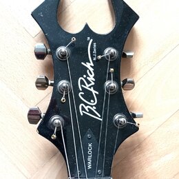 Černá hlava elektrické kytary s výrazným, ostře zakončeným tvarem. Na povrchu je bílý nápis B.C. Rich, N.J. Series a v dolní části označení WARLOCK.…