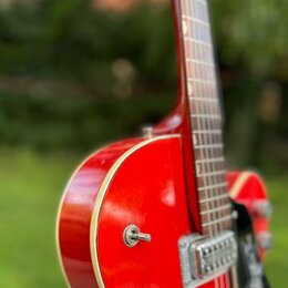 Červená polodublová elektrická kytara s bílým lemováním hran. Na těle jsou vidět dva stříbrné humbuckery a černý plecháč. Povrch laku je lesklý, bez…