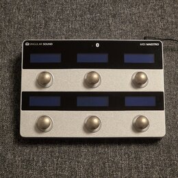 Stříbrný MIDI kontrolér s nápisy SINGULAR SOUND a MIDI MAESTRO. Zařízení má dvě řady tří modrých displejů a dvě řady tří kulatých kovových tlačítek.…