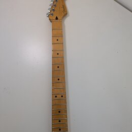 Světle hnědý javorový krk elektrické kytary s prázdnými otvory pro pražce. Na hlavě je viditelné logo Fender a nápis MADE IN USA. Krk je vybaven chro…