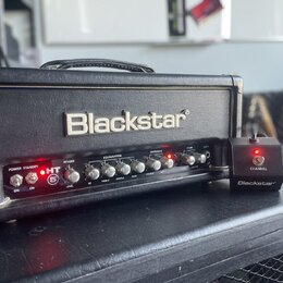 Černý kytarový zesilovač s nápisem Blackstar na předním panelu. Pod logem se nachází ovládací prvky s nápisy POWER, STANDBY, HT 5, REVERB (LEVEL), EQ…